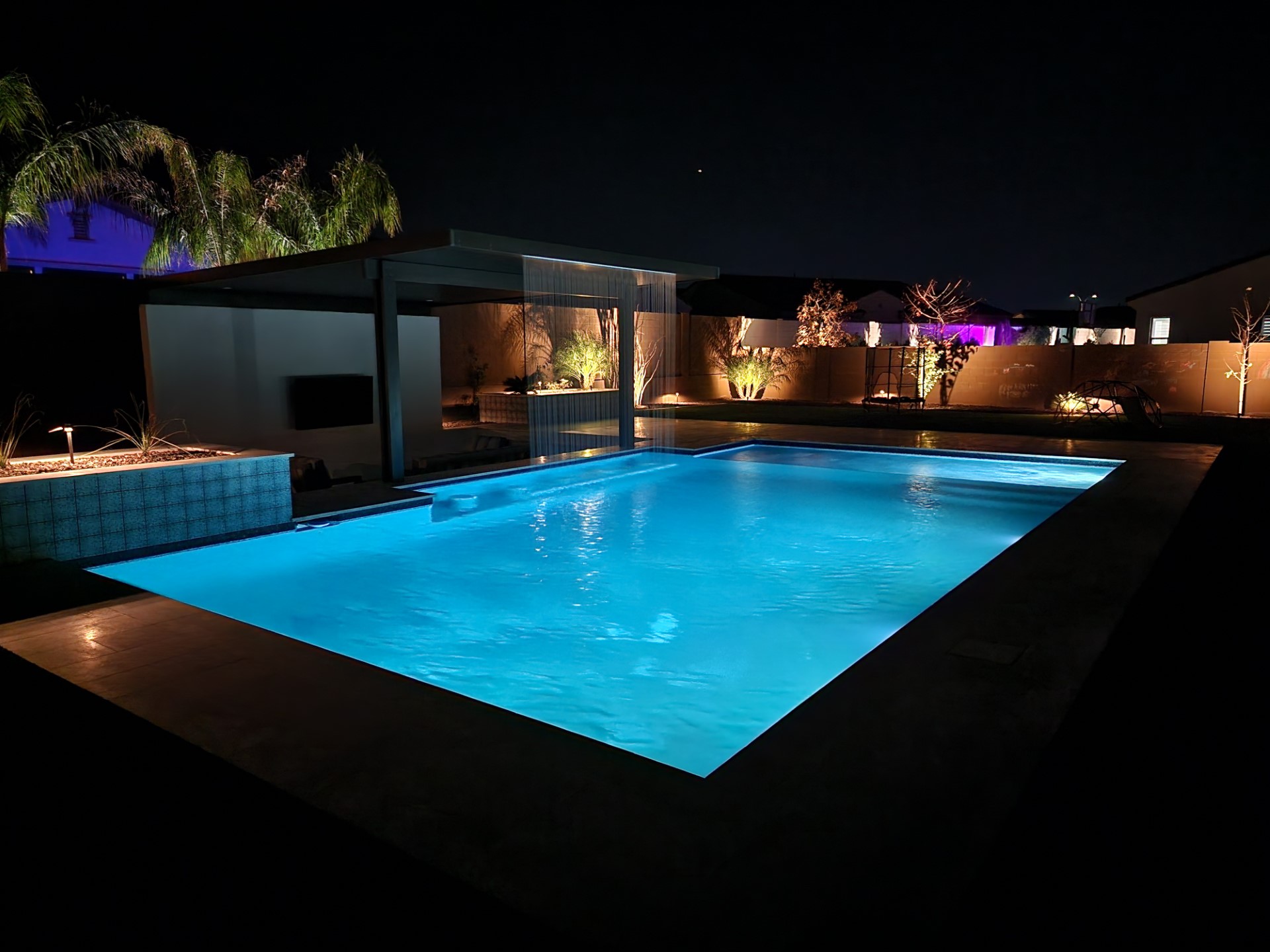 Modern illuminated swimming pool with water curtain and premium backyard lighting